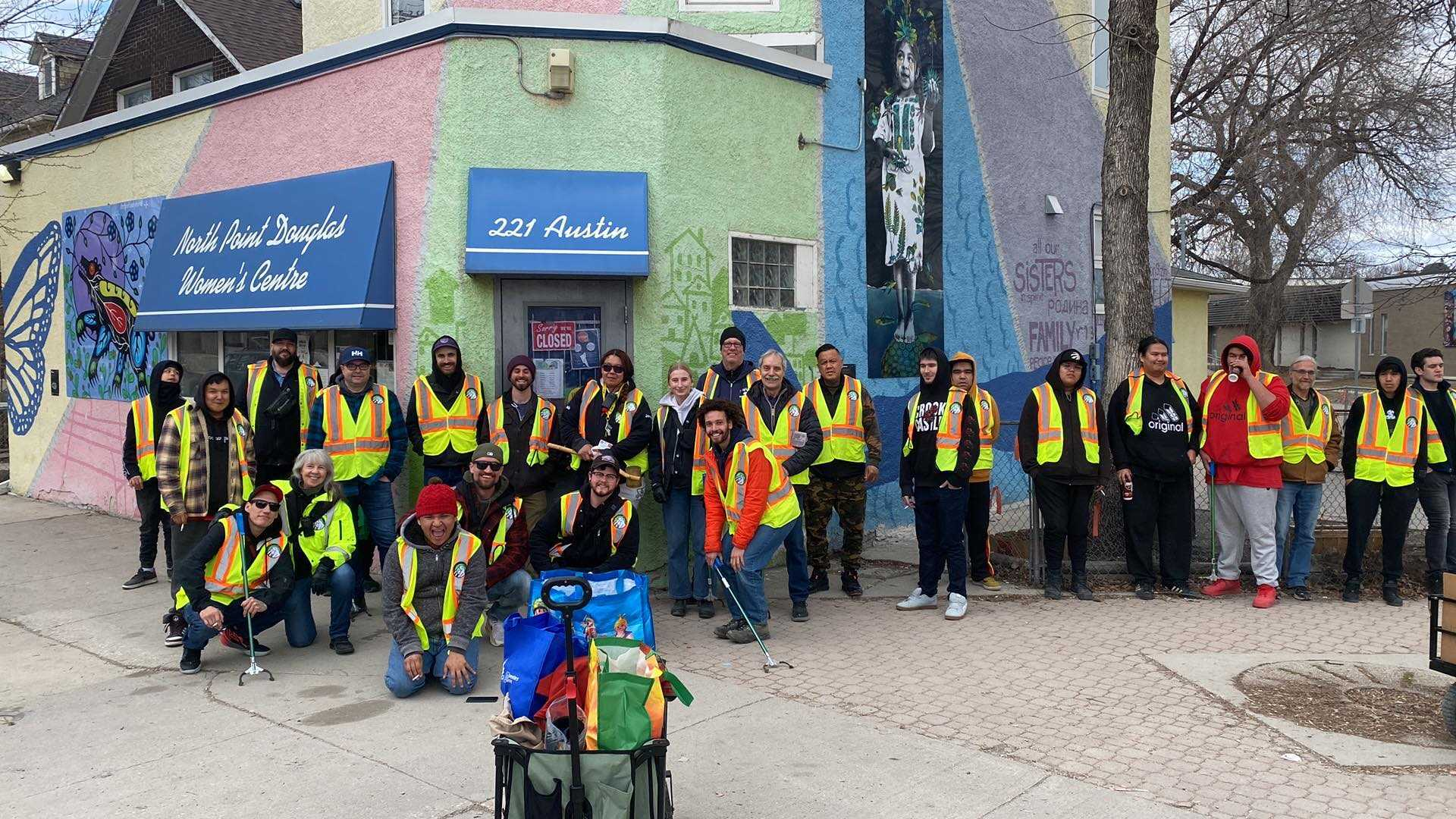 Horizontal photo of about 25 people in neon yellow vests standing in a line outside the North Point Douglas Woomen's Centre before the Sunday patrol