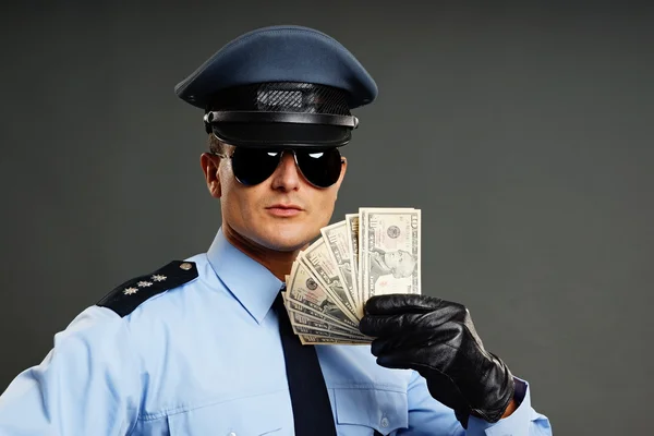 Stock photo of a cop wearing aviators, poilce uniform hat, and black gloves displaying a bunch of bills