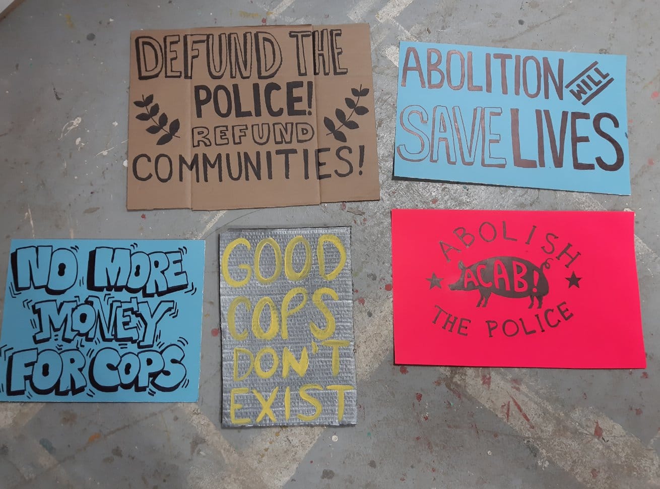 Photo of five signs on ground with messages that say "abolition saves lives" and "no more money for cops"