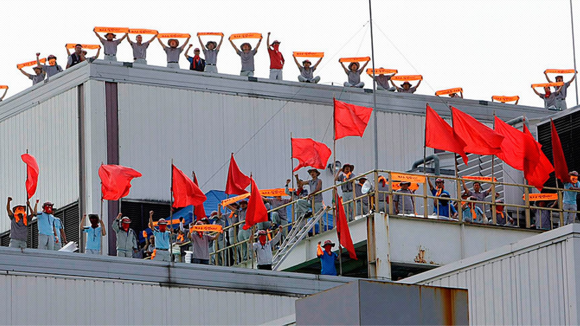 Photo of many workers on top of South Korean factory with red flags and banners