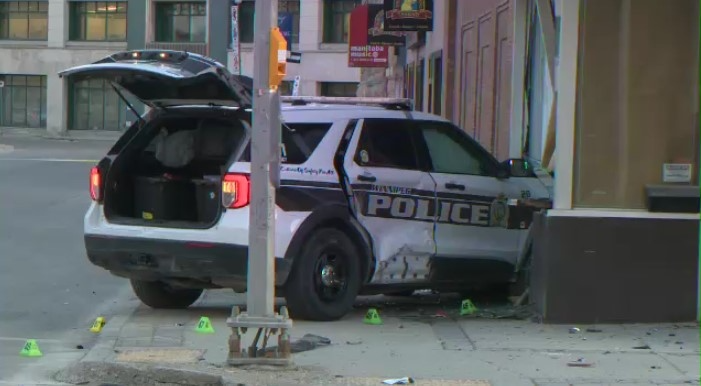 A photo of a police SUV that has slammed into a wall. Its trunk is open and its side crumpled. Small yellow cones are on the ground.