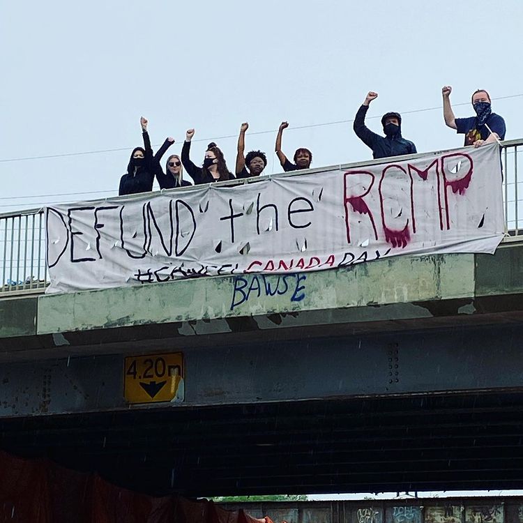 members of winnipeg police cause harm holding a defund the police banner over a bridge